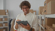 © Krakenimages.com - Man holding tablet and stylus writing inventory in warehouse among cardboard boxes and shelving; entrepreneurial satisfaction.