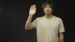 © Krakenimages.com - Young hispanic man raises right hand with palm facing camera in studio, wearing beige tshirt and neutral expression; calm introspection.