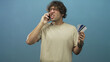 © Krakenimages.com - Man holding phone to ear with one hand and fanning creditcard in the other, grimacing and shouting while wearing glasses and a beige t shirt in studio; financial stress frustration.