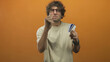 © Krakenimages.com - Man wearing glasses, holding creditcard and clenching fist toward camera while gritting teeth in orange studio; frustration.