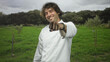 © Krakenimages.com - Man chef in white jacket smiling taps wristwatch while standing among young trees in a forest field, pointing with right hand; confidence.