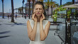 © Krakenimages.com - Woman holding jaw with hand on cheek in restaurant terrace on street by promenade, eyes closed and wincing for toothache; discomfort medical.