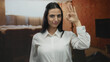 © Krakenimages.com - Young hispanic woman in white shirt making 'ok' gesture at an indoor construction site, surrounded by red brick walls, exuding confidence and positivity.