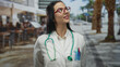 © Krakenimages.com - Woman doctor smiling on a street terrace, wearing a stethoscope and uniform, with outdoor restaurant and coffee shop ambiance blending medical professionalism and urban lifestyle.