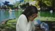 © Krakenimages.com - Woman in white sweater covers face anxiously in a green park with ducks, set against a vivid outdoor background, capturing youthful hispanic emotion in nature setting.