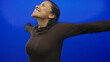 © Krakenimages.com - Woman smiling joyfully against a vibrant blue background with arms spread wide in an expression of freedom and happiness.