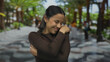 © Krakenimages.com - Hispanic woman embraces herself with a smile in a vibrant outdoor street setting lined with palm trees, creating a sense of joy and tranquility.