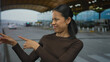 © Krakenimages.com - Young woman stands outside an airport terminal, looking thoughtful against a backdrop of a modern architectural roof and distant vehicles.