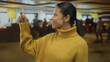 © Krakenimages.com - Hispanic woman in yellow sweater points indoors at a busy hotel reception area with people engaging in background activities in a warmly lit environment.