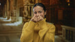 © Krakenimages.com - Young hispanic woman in a yellow sweater makes a heart gesture with her fingers inside a church, smiling warmly and bringing a sense of joy and connection to the sacred setting.