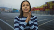 © Krakenimages.com - Young woman with striped shirt stands concerned at port with shipping containers in the background suggesting an outdoor seaside location.