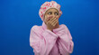 © Krakenimages.com - Young woman in pink bathrobe with shower cap covers mouth against blue background showing surprise and emotion.