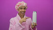 © Krakenimages.com - Hispanic woman in bathrobe makes an ok gesture while holding a shampoo bottle against a vibrant pink background.