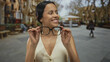 © Krakenimages.com - Young hispanic woman smiling while adjusting glasses on a lively street outdoors, capturing the essence of urban lifestyle in broad daylight.