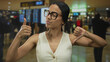 © Krakenimages.com - Woman giving thumbs up and down indoors at airport terminal wearing glasses, expressing mixed feelings in vibrant scene with modern architecture backdrop.
