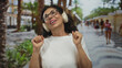 © Krakenimages.com - Woman enjoying music with headphones and smiling outdoors on a vibrant street lined with palm trees, embodying a joyful and carefree mood enhanced by the natural setting.