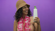 © Krakenimages.com - Middle-aged hispanic woman in a bikini with a hawaiian lei and hat smiling against an isolated purple background holding a bottle.