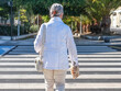 © luciano - Rear view of a casually dressed gray-haired senior woman crossing a city street on a pedestrian crossing