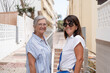 © luciano - Two happy senior women smiling to the camera while walking together on a sunny residential street. The elderly friends expressing joy, friendship, and an active lifestyle