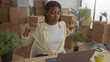 © Krakenimages.com - African american woman typing on laptop among cardboard moving boxes in building, glancing at wrist and gesturing with hands; focus moving day planning.