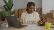 © Krakenimages.com - African american woman presses calculator and types on laptop at table in building; budgeting concentration.