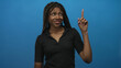 © Krakenimages.com - African american woman wearing black polo and cross necklace pointing index finger in blue studio; playful curiosity.