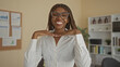 © Krakenimages.com - African american woman with glasses and braided hair, hands under chin smiling while seated in an office with shelves and corkboards; confidence charm.