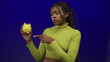 © Krakenimages.com - African american woman wearing lime turtleneck points finger to yellow piggybank in studio with blue backdrop; saving money caution.