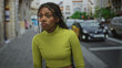 © Krakenimages.com - African american woman with braided hair wearing lime turtleneck and visible midriff standing on a city street near cars and buildings; quiet determination.