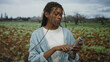 © Krakenimages.com - Woman wearing glasses and denim shirt points finger to phone while holding smartphone in field with green crops under cloudy sky; focus attention.