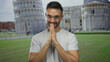 © Krakenimages.com - Young man smiling in front of pisa tower in italy with hands clasped together in gratitude, showcasing a serene expression and vivid historical landmark.