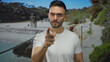 © Krakenimages.com - Young hispanic man pointing at camera with a serious expression on a beach, surrounded by sea and nature, wearing a casual white shirt outdoors.