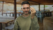 © Krakenimages.com - Young man with a beard gesturing expressively on an outdoor terrace in a restaurant with wooden tables and chairs, conveying emotions in a casual setting.