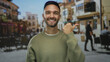 © Krakenimages.com - Young man smiling on city street pointing with thumb in urban outdoor setting with buildings and cafes in background, showcasing casual happy mood in lively environment.
