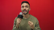 © Krakenimages.com - Young man with microphone giving an interview against red background showcasing expressive gestures and focused communication skills in a studio setting.