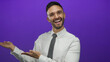 © Krakenimages.com - Young hispanic man smiling and presenting with open hands against a vibrant purple background in formal attire.