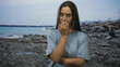 © Krakenimages.com - Woman biting fingernails with hand to mouth on rocky street near the seaside, arms crossed and tense expression, casual t shirt visible; anxiety.