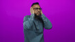 © Krakenimages.com - Man covering ears with hands in studio against bright magenta purple wall wearing denim shirt and glasses; discomfort.