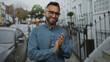 © Krakenimages.com - Man clapping hands on street sidewalk next to parked cars and iron railings, wearing denim shirt and glasses; gentle contentment.