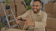 © Krakenimages.com - Man holding a game controller in a new home building surrounded by packed cardboard boxes and a ladder, smiling and leaning forward; happiness comfort.