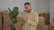 © Krakenimages.com - Man holding smartphone smiling with fist pump in building stacked with moving boxes and houseplant; moving day joy.