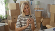 © Krakenimages.com - Woman types on laptop and checks smartphone amid packed moving boxes in building; moving transition contentment.