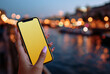 © Sher - a close-up of an iphone in the hand, showing its screen with blurred city lights and nature background