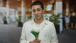 © Krakenimages.com - Young man in white shirt holding tulips stands outdoors with blurred background, exuding a cheerful and serene vibe, providing a sense of tranquility in a lively setting.