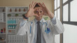 © Krakenimages.com - Young hispanic doctor in uniform making heart symbol with hands in hospital room with shelves of medical supplies and large windows