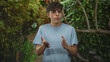 © Krakenimages.com - Teenage boy gesturing with hands while speaking in forest walkway with wooden railing and dense foliage; thoughtful reflection.