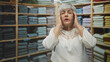 © Krakenimages.com - Woman with hand to temple and hand on hip among stacked folded sweaters and linens in a clothing store building; frustration.
