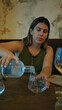 © Krakenimages.com - Woman pours water from bottle into a stemless glass at a restaurant table inside a building, hand steady and focused on the glass; calm contemplation.