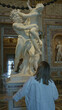 © Krakenimages.com - Young woman with hand on railing leaning forward viewing large marble statue of two figures in ornate gallery building; art appreciation awe.