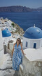 © Krakenimages.com - Woman in blue sundress waving hand and leaning on railing beside white church dome building in santorini; holiday relaxation serenity.